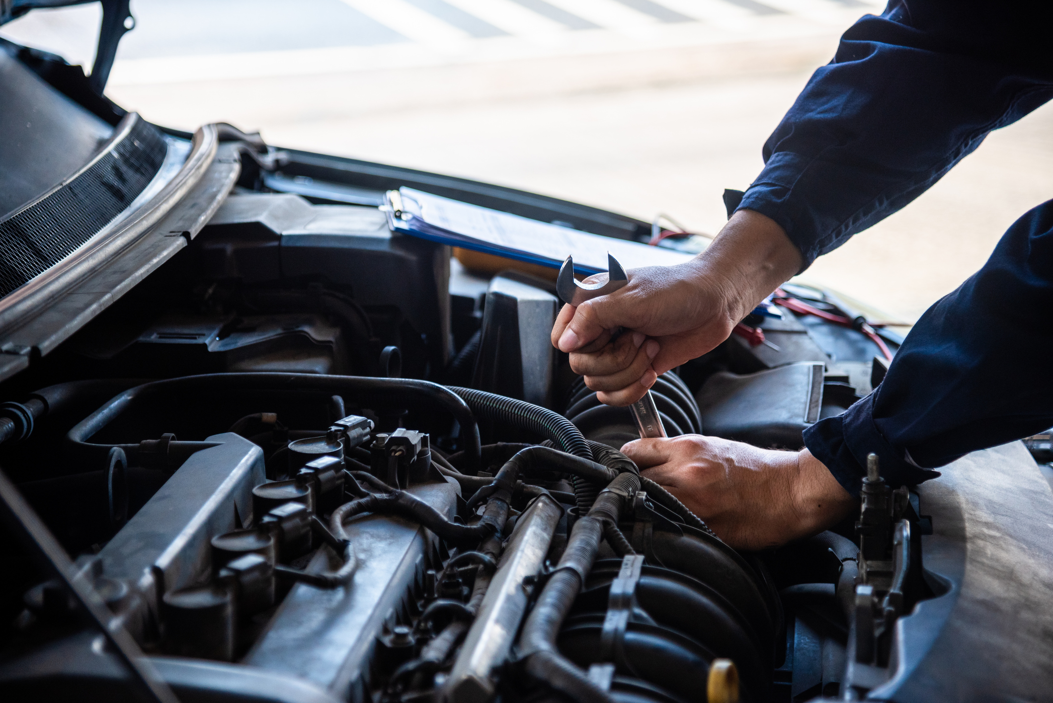 Mechanic working on a car engine in a garage, holding a tool in his hand