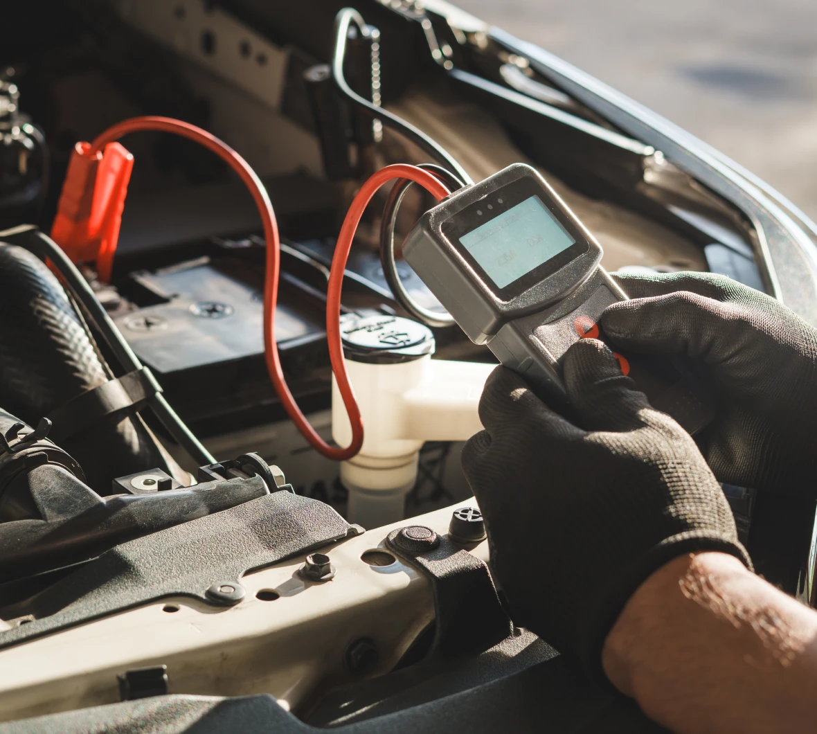 Person wearing gloves and using a digital multimeter to check the voltage of a car battery